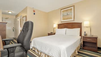 A hotel room with a bed, a chair, a desk, and a nightstand with lamps.