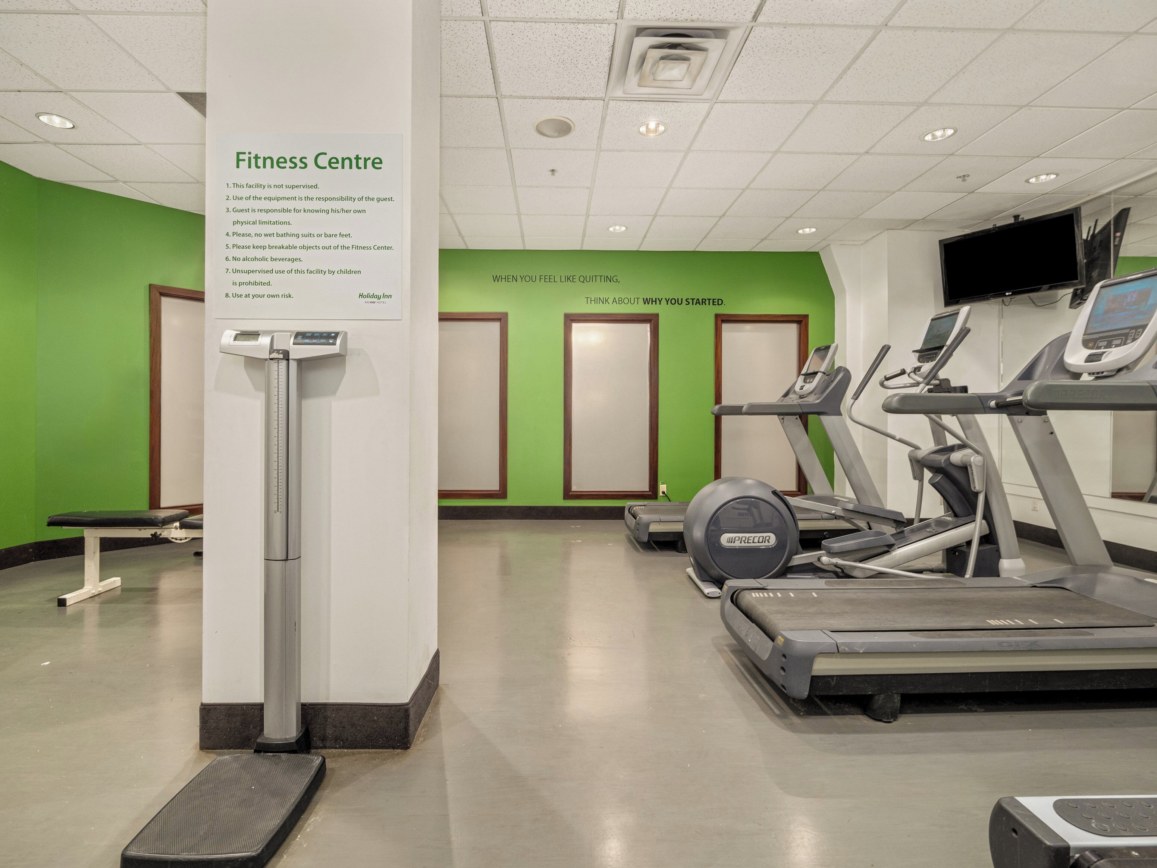 Une salle de sport équipée de tapis de course, d’une balance numérique et d’un panneau affichant les règles.