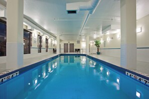 Una piscina interior con marcas claras para carriles, una silla de salvavidas y un cartel que indica que no hay salvavidas de servicio.