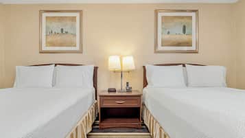 A hotel room with two beds, a striped carpet, and two framed landscape paintings on the walls.