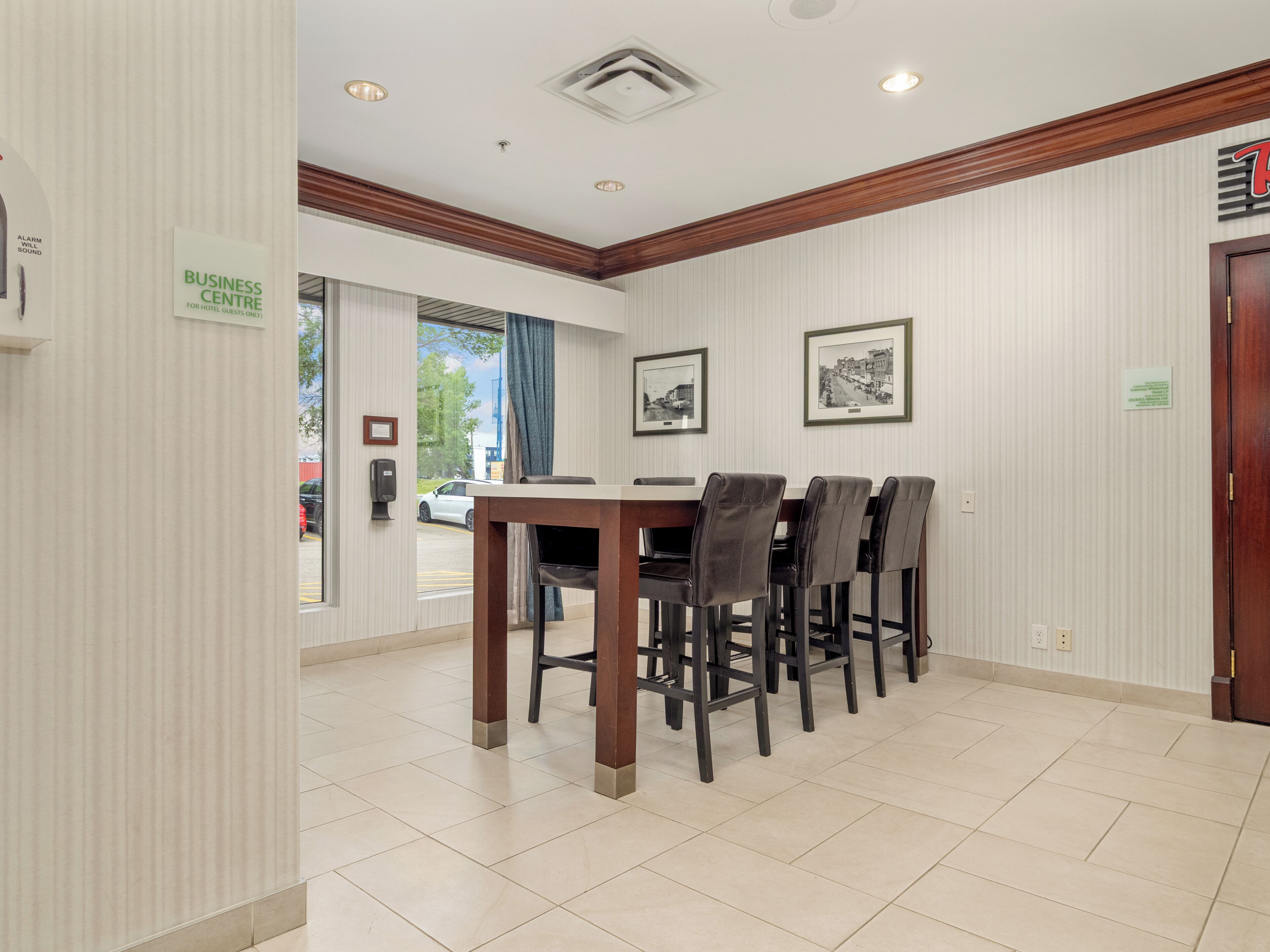 A business center with a dining area, including a table and chairs, framed pictures on the wall, and a sign indicating it is for hotel guests only.