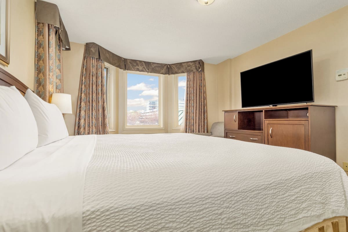 A hotel room with a large bed, a flat-screen TV, a wooden cabinet, and a window with curtains.