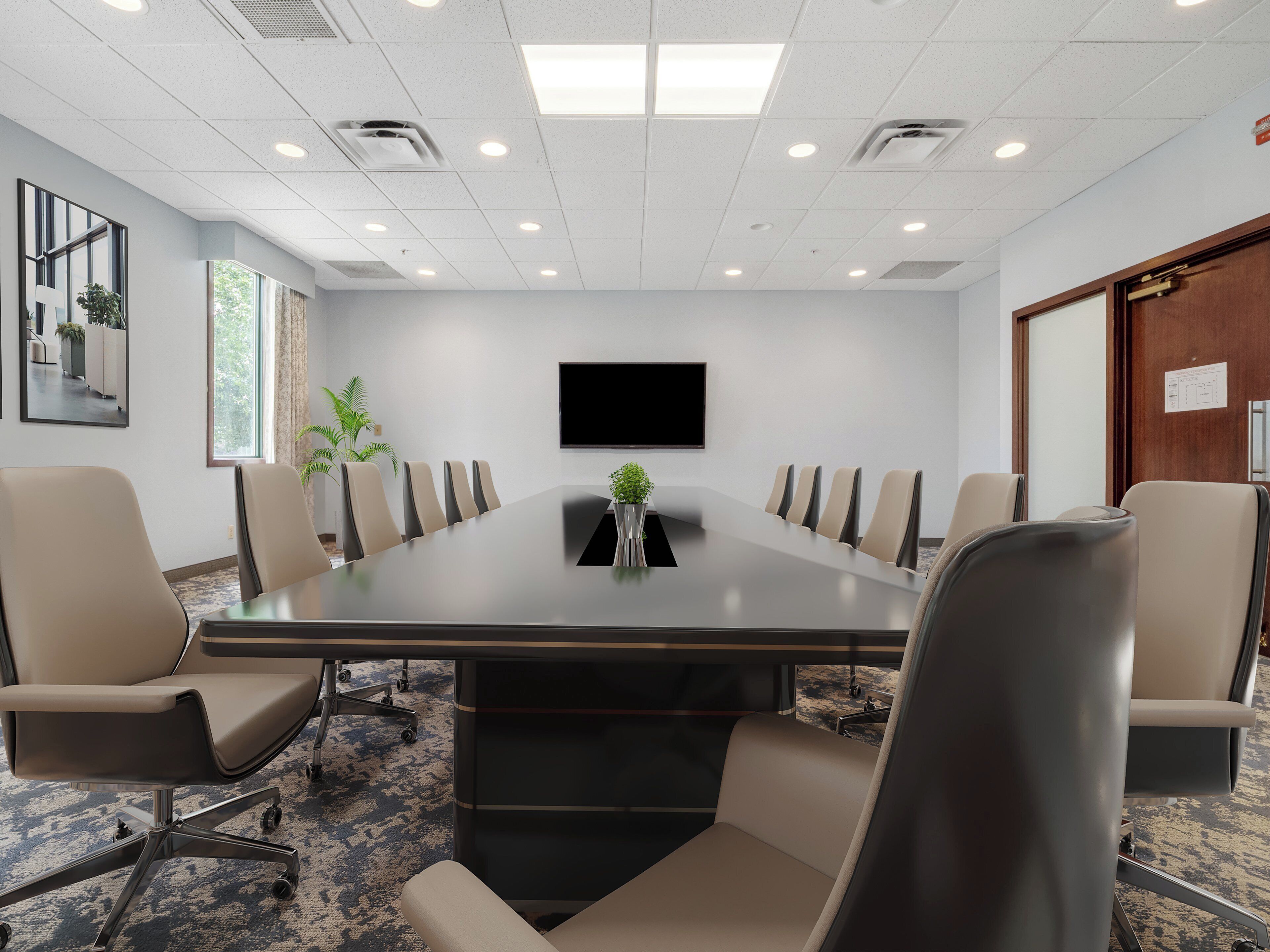 Une salle de conférence avec une longue table, plusieurs chaises, un téléviseur fixé au mur et une porte avec une pancarte.