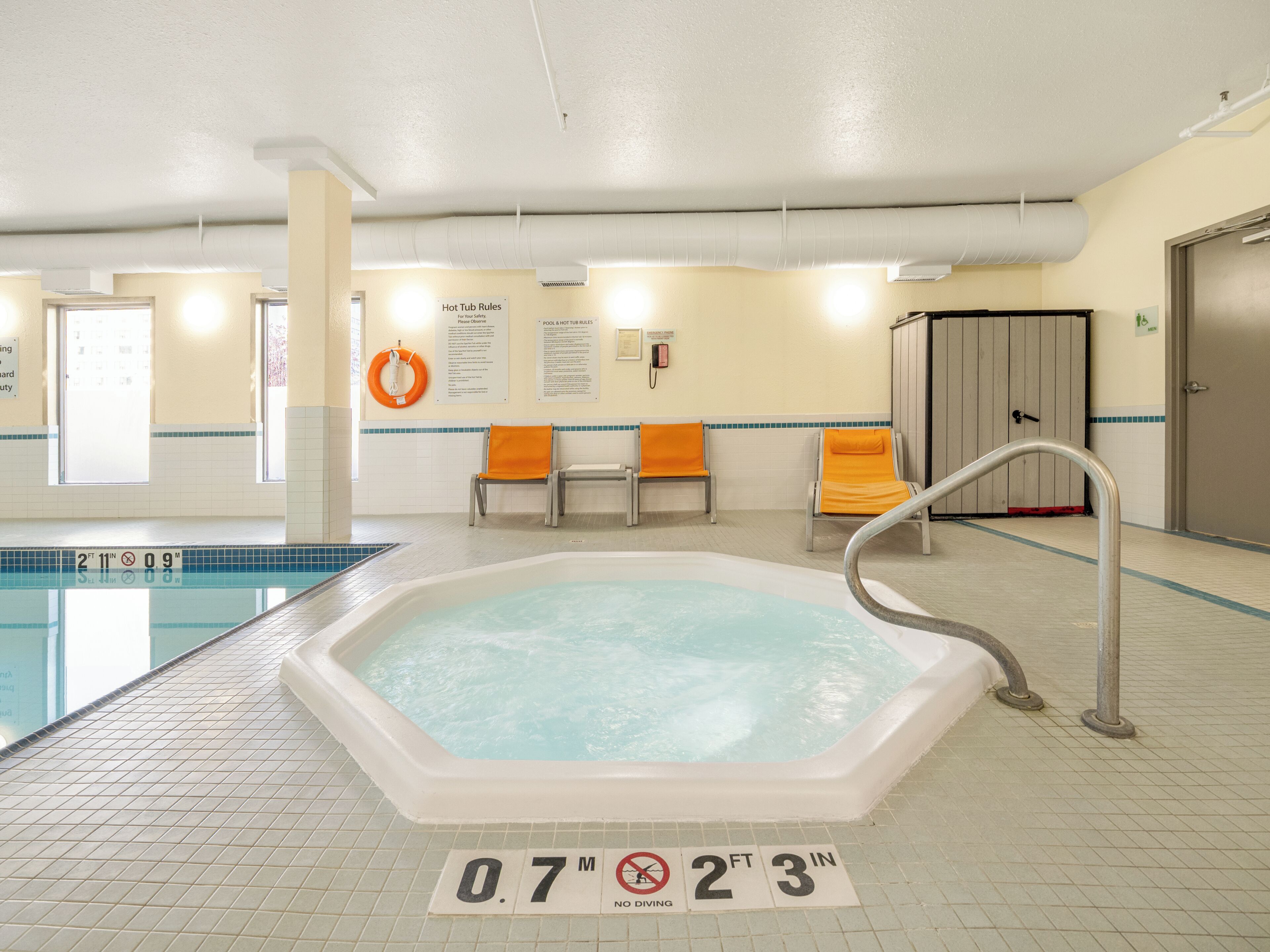 A pool area with a hot tub, lounge chairs, and safety signage.