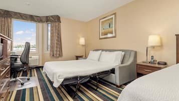 A hotel room with a bed, a desk, a chair, a lamp, and a painting on the wall.