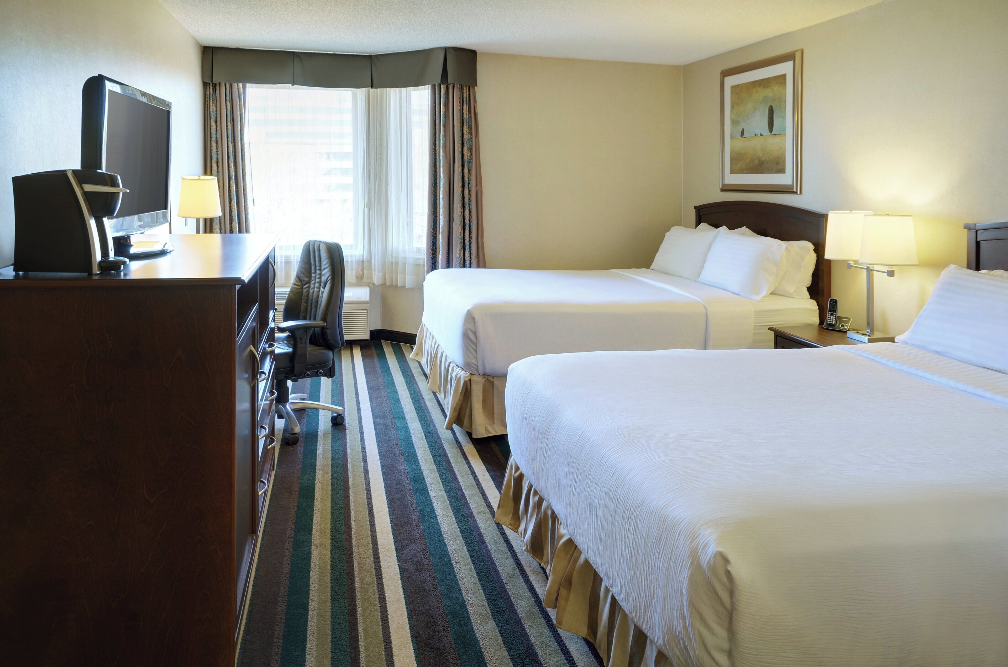Een hotelkamer met twee bedden, een bureau met een computer, een stoel en een televisie.