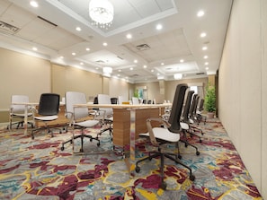 Une salle de conférence avec une longue table, de nombreuses chaises, un bureau en bois et un lustre.