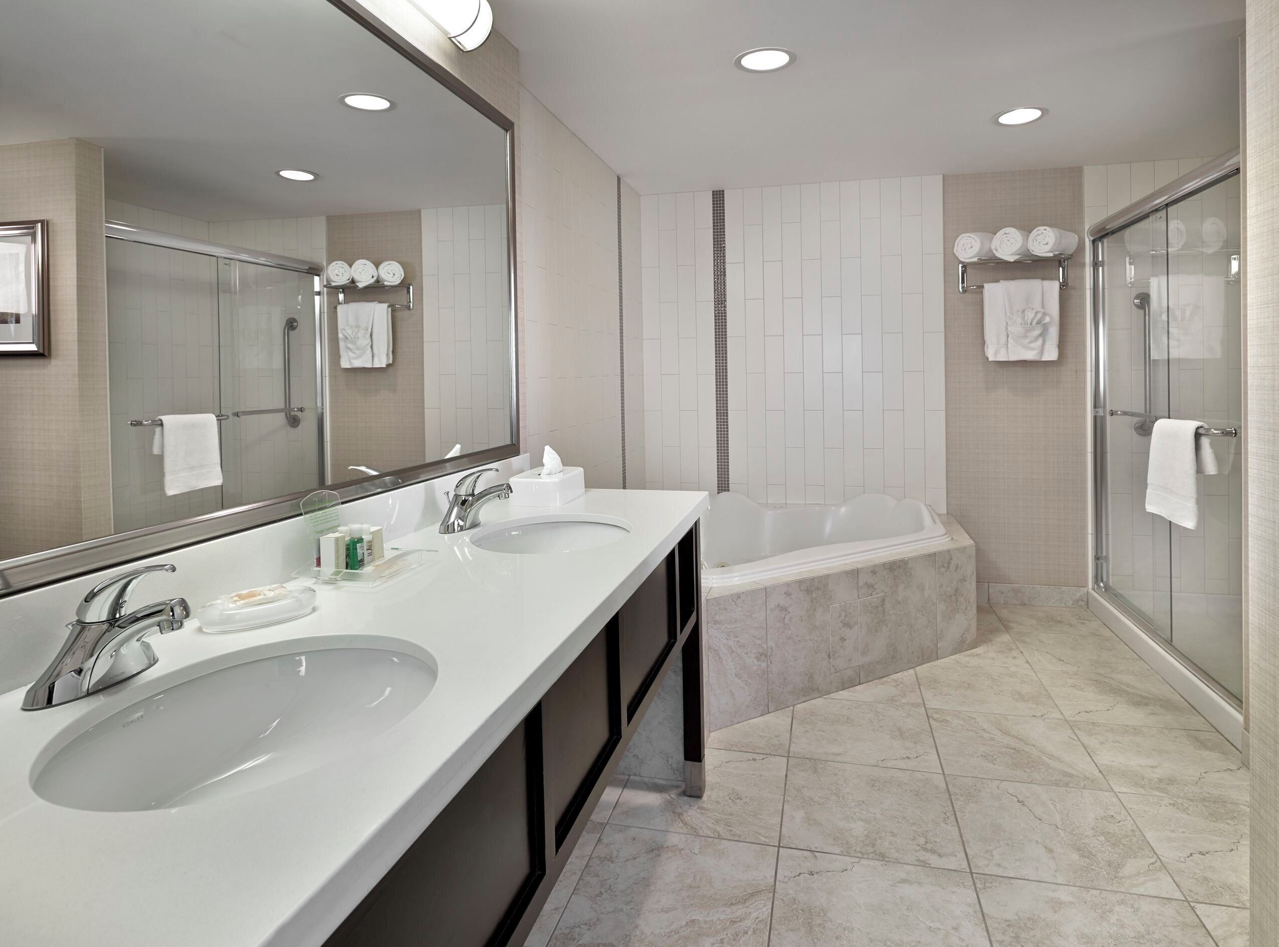 Une salle de bain moderne avec deux lavabos, un grand miroir, une baignoire et une douche à parois de verre.