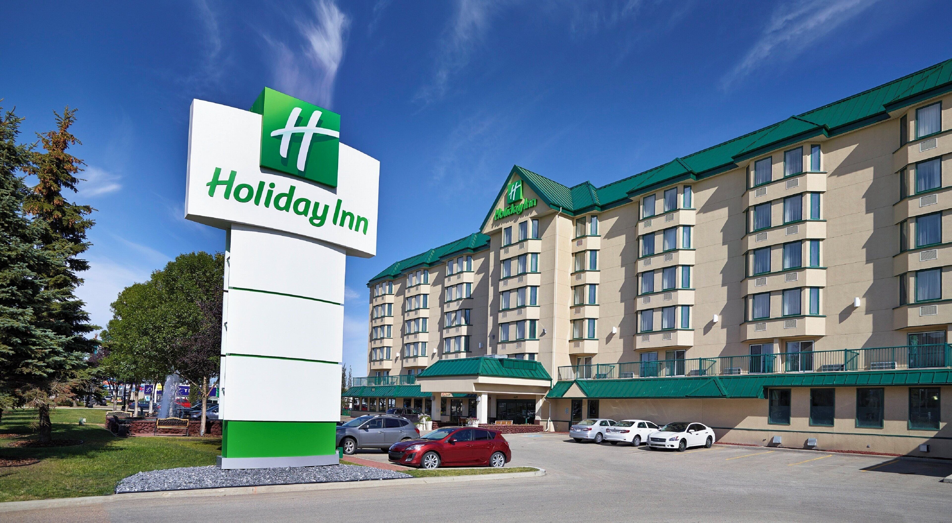 Un hotel Holiday Inn con un letrero grande, varios espacios de estacionamiento y un edificio con techo verde.