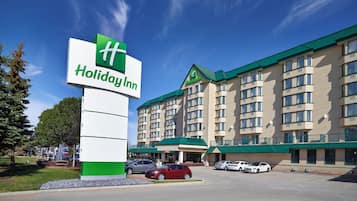 A Holiday Inn hotel with a large sign, multiple parking spaces, and a green-roofed building.