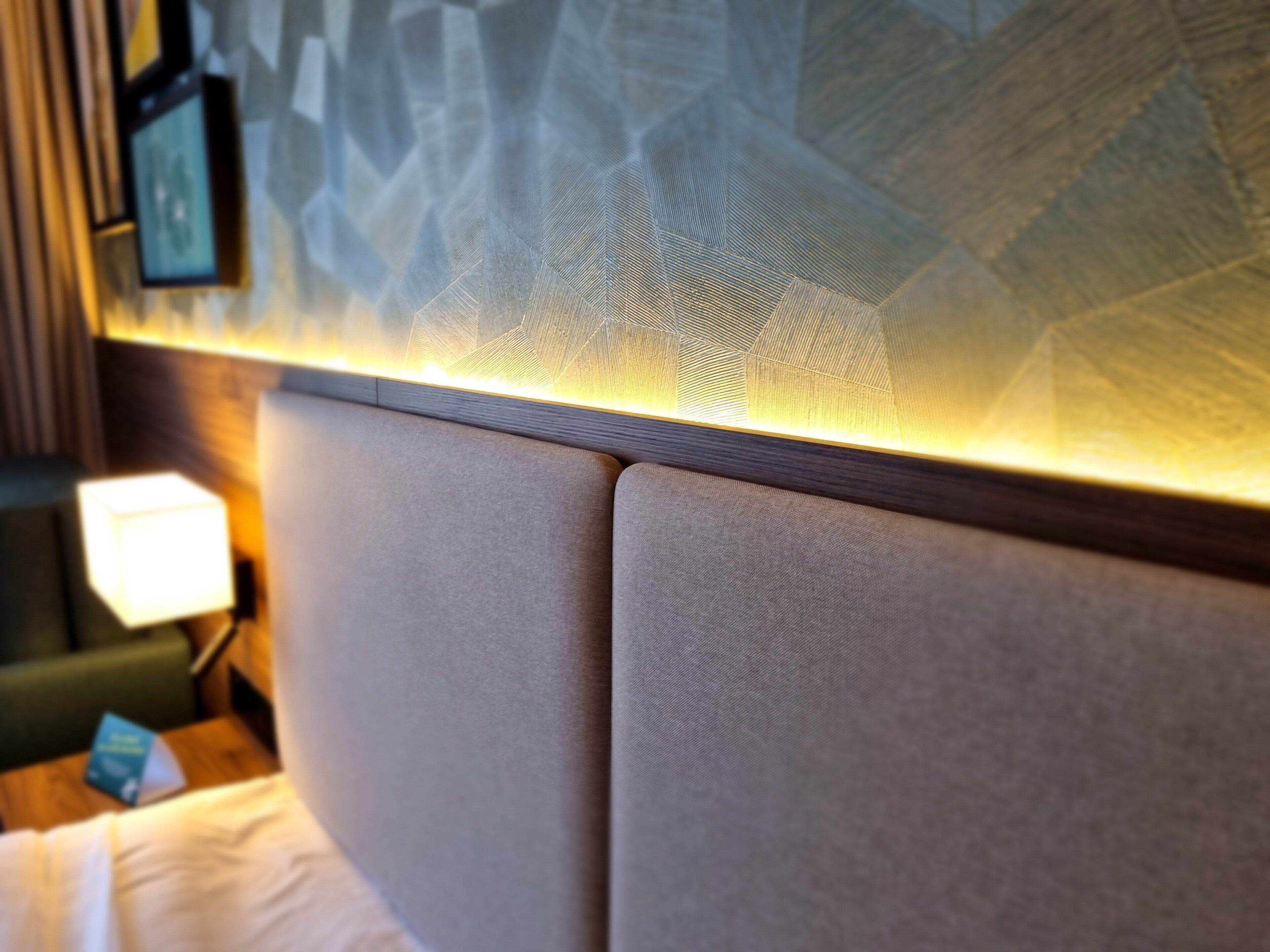 Een detailopname van een hoofdeinde in een kamer, met een structuurwand en een wandlamp.