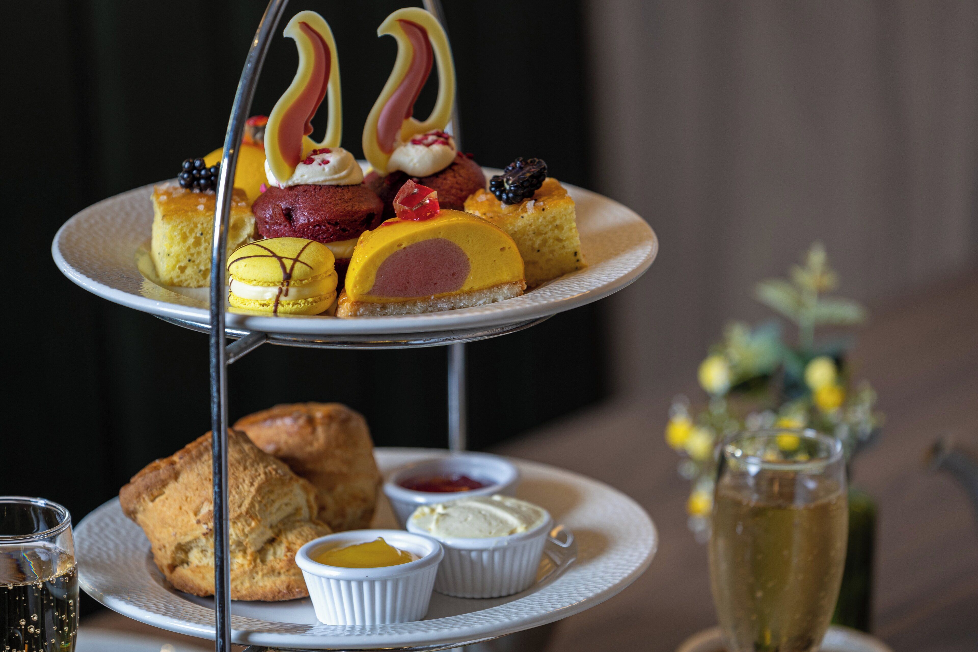 A three-tiered dessert stand with various pastries and desserts, accompanied by small bowls of cream and a glass of champagne.