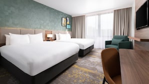 A hotel room with two beds, a desk, a chair, a TV, and a window with curtains.