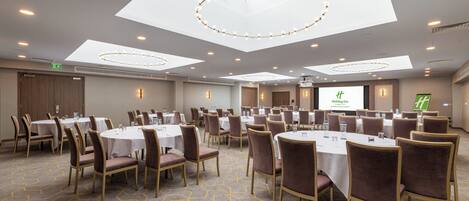 Une salle de conférence équipée de tables rondes, de chaises et d’un grand écran diffusant une présentation.