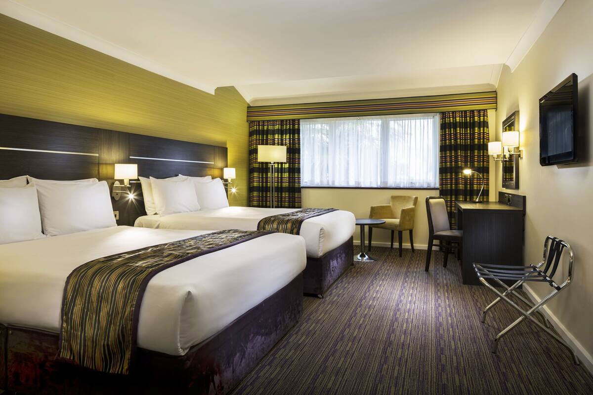 A hotel room with two beds, a desk, a chair, and a TV.