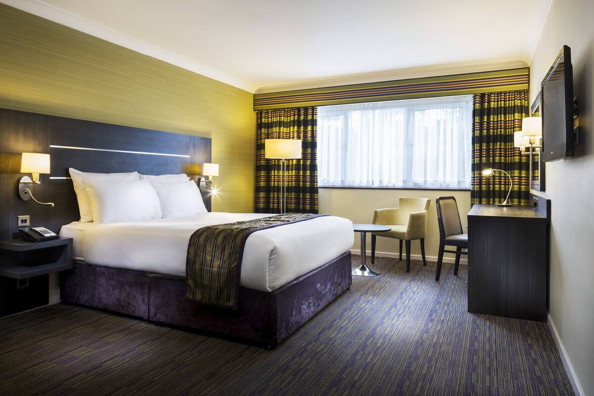 A hotel room with a large bed, bedside lamps, a desk with a chair, and a television.