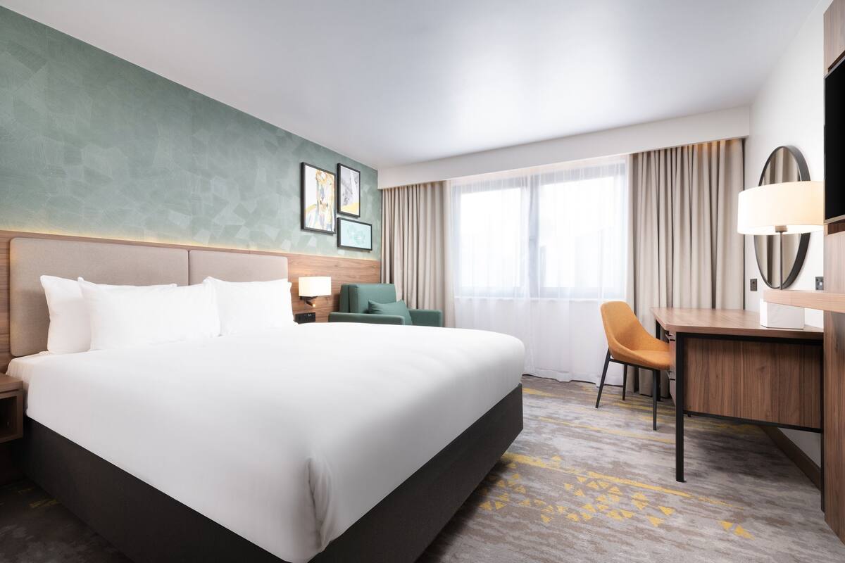 A hotel room with a large bed, a desk, a chair, a TV, and a window with curtains.