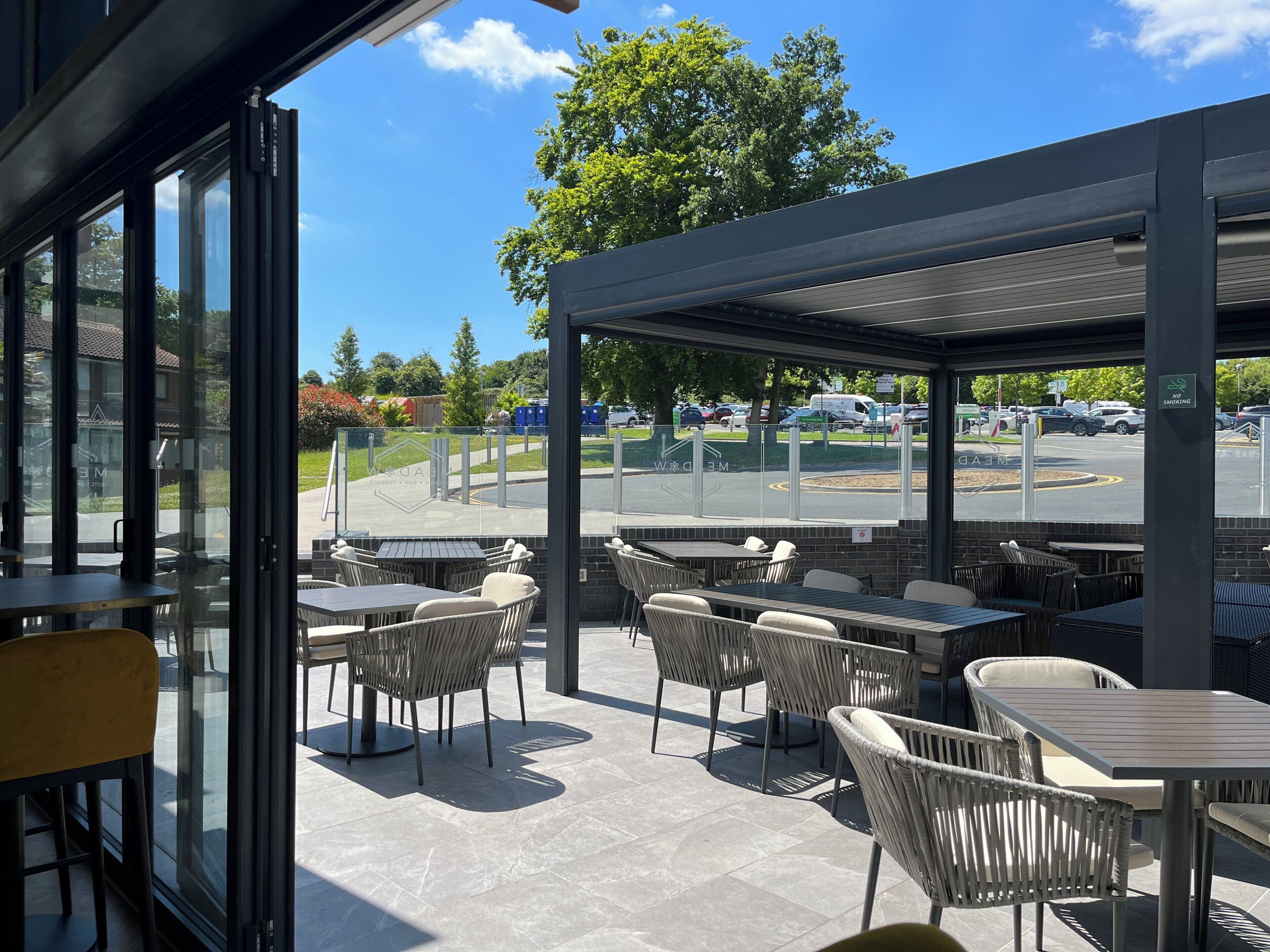 An outdoor seating area with tables and chairs, a covered section, and a view of a parking lot.