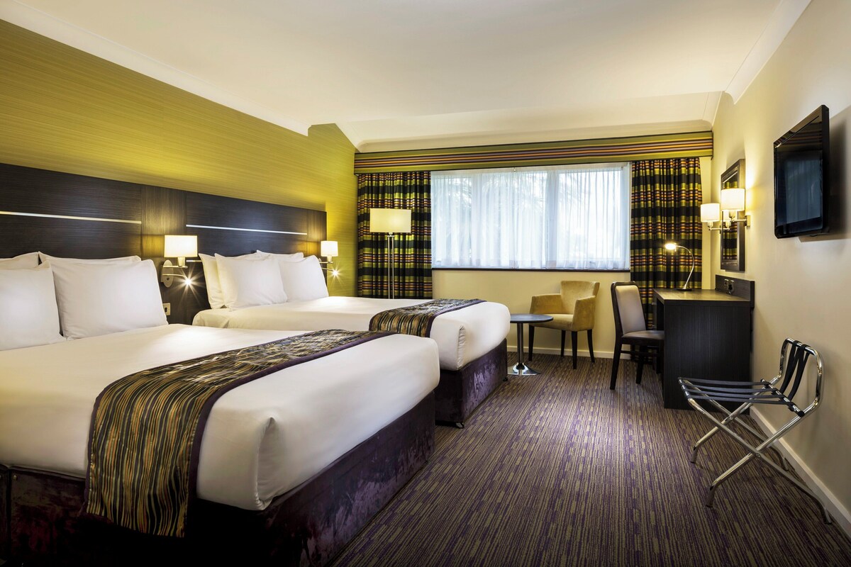 Une chambre d’hôtel avec deux lits, un bureau, une chaise et un téléviseur.