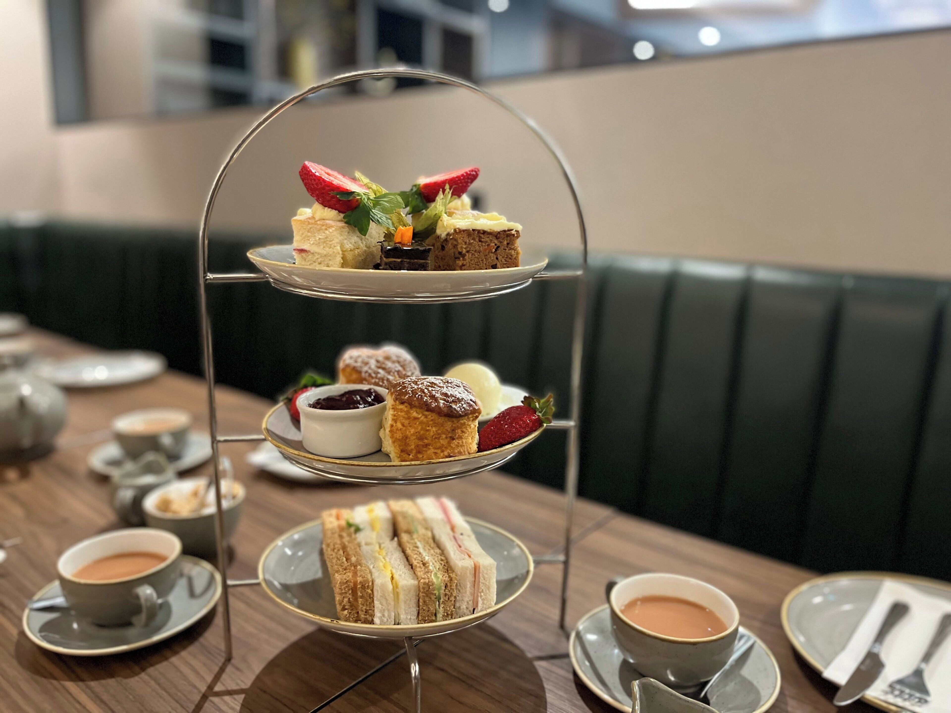 Un soporte de tres niveles para postres con sándwiches, scones y pasteles sobre una mesa en un restaurante.