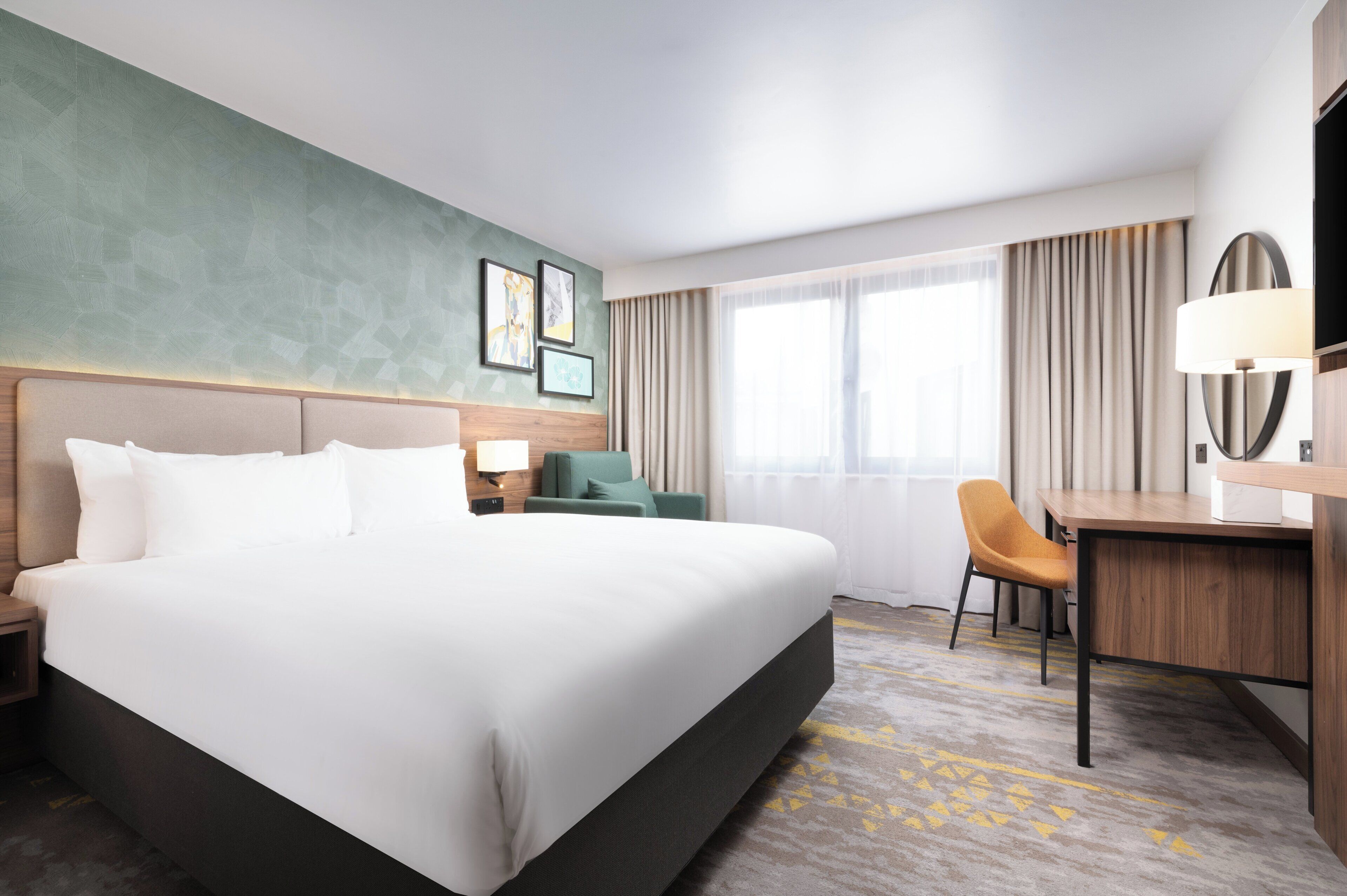 A hotel room with a large bed, a desk, a chair, and a TV.