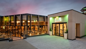 A Holiday Inn hotel with a modern glass facade, outdoor seating area, and a well-lit entrance.