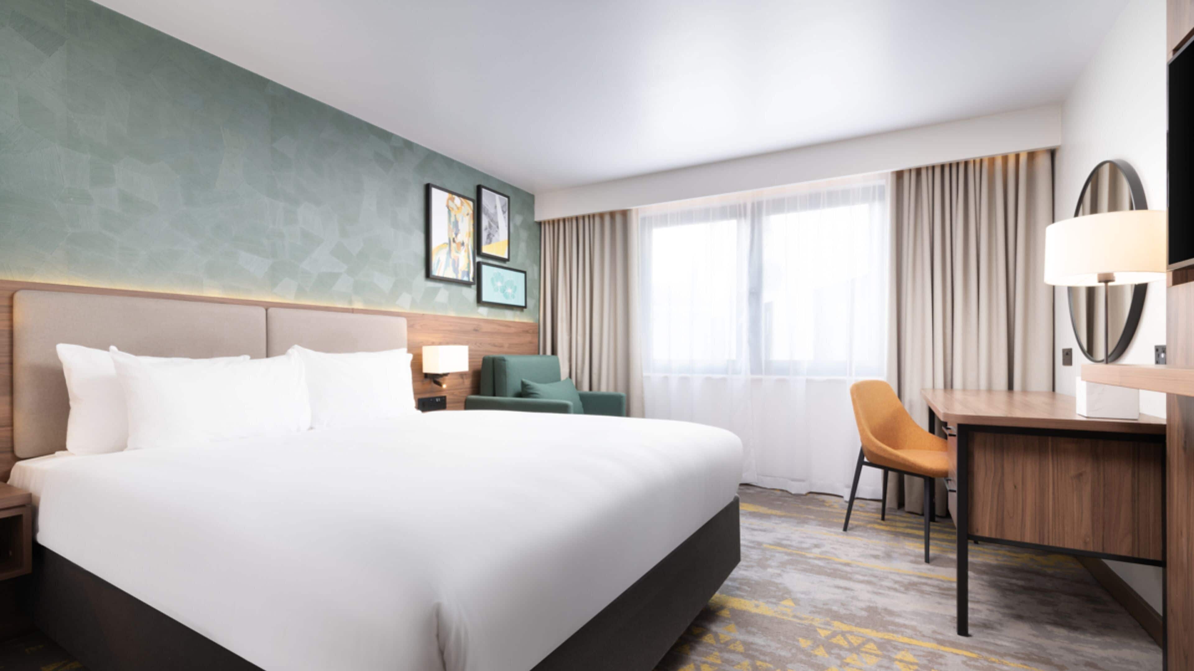 A hotel room with a large bed, a desk, a chair, and a window with curtains.