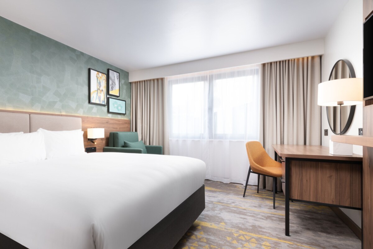 Une chambre d’hôtel avec un grand lit, un bureau, une chaise et une fenêtre avec des rideaux.