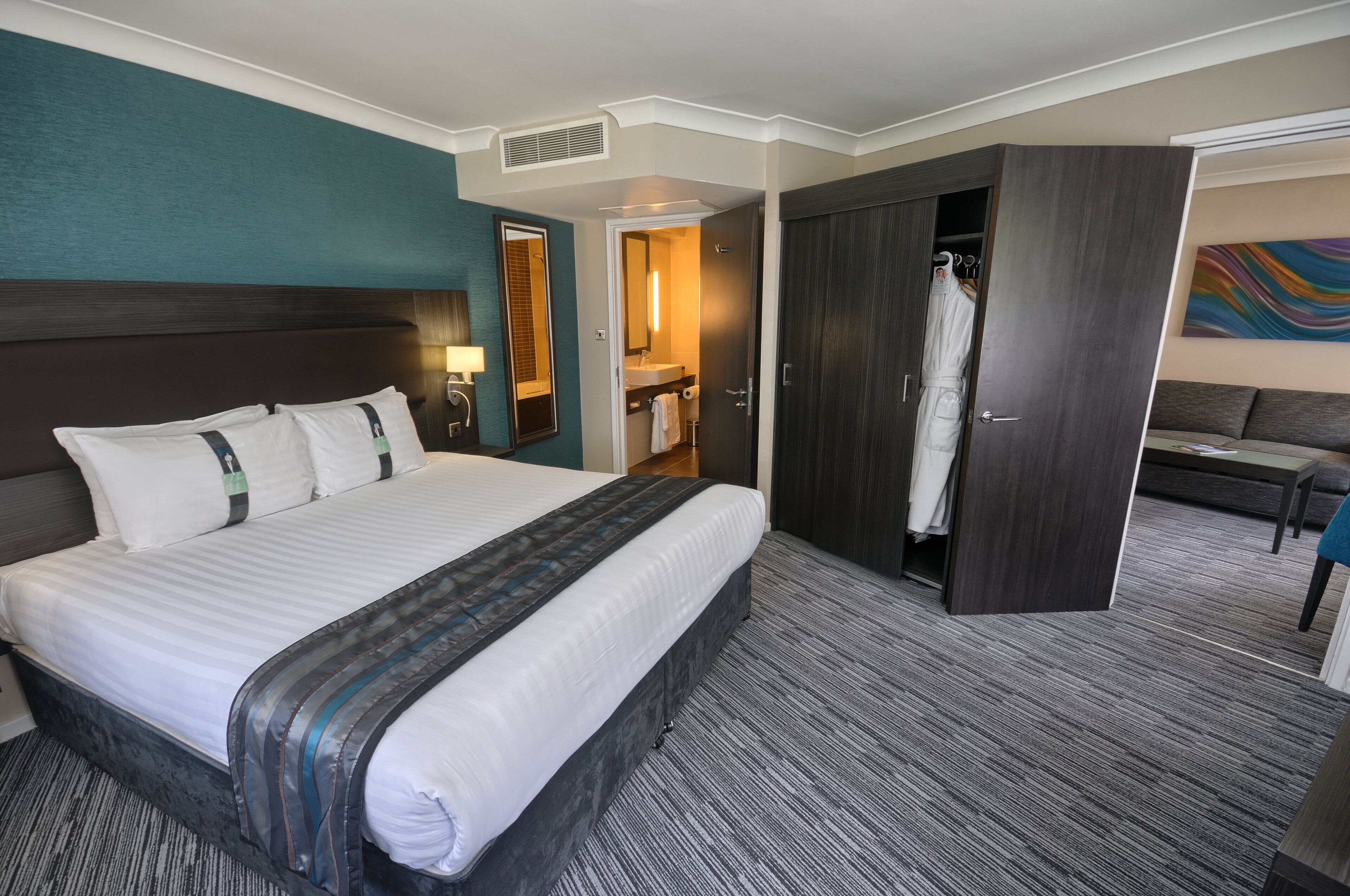 A hotel room with a large bed, a wardrobe, a bathroom, and a seating area.