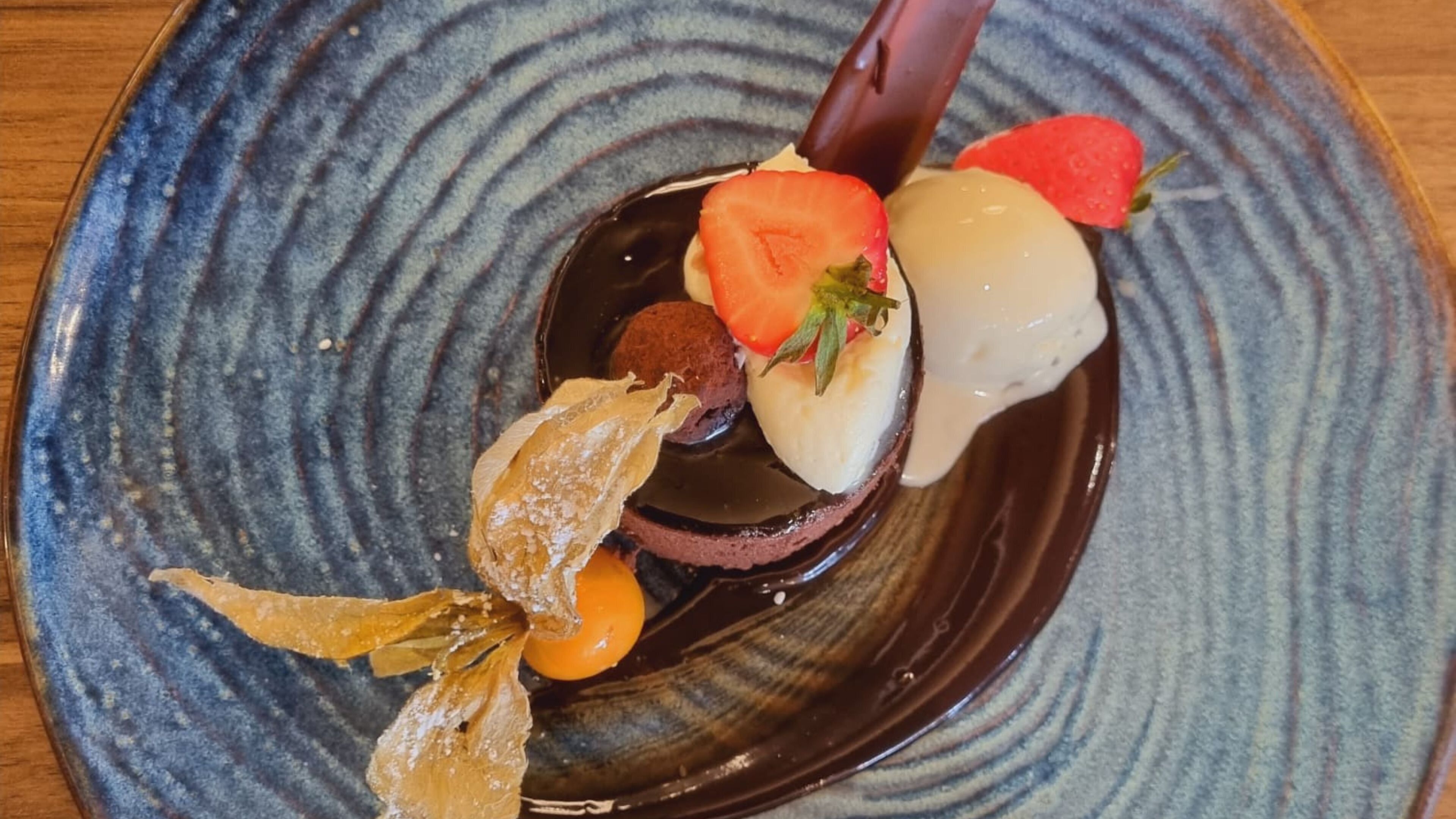 A dessert plate with various items including a chocolate sphere, a strawberry, a slice of cake, and some decorative elements.