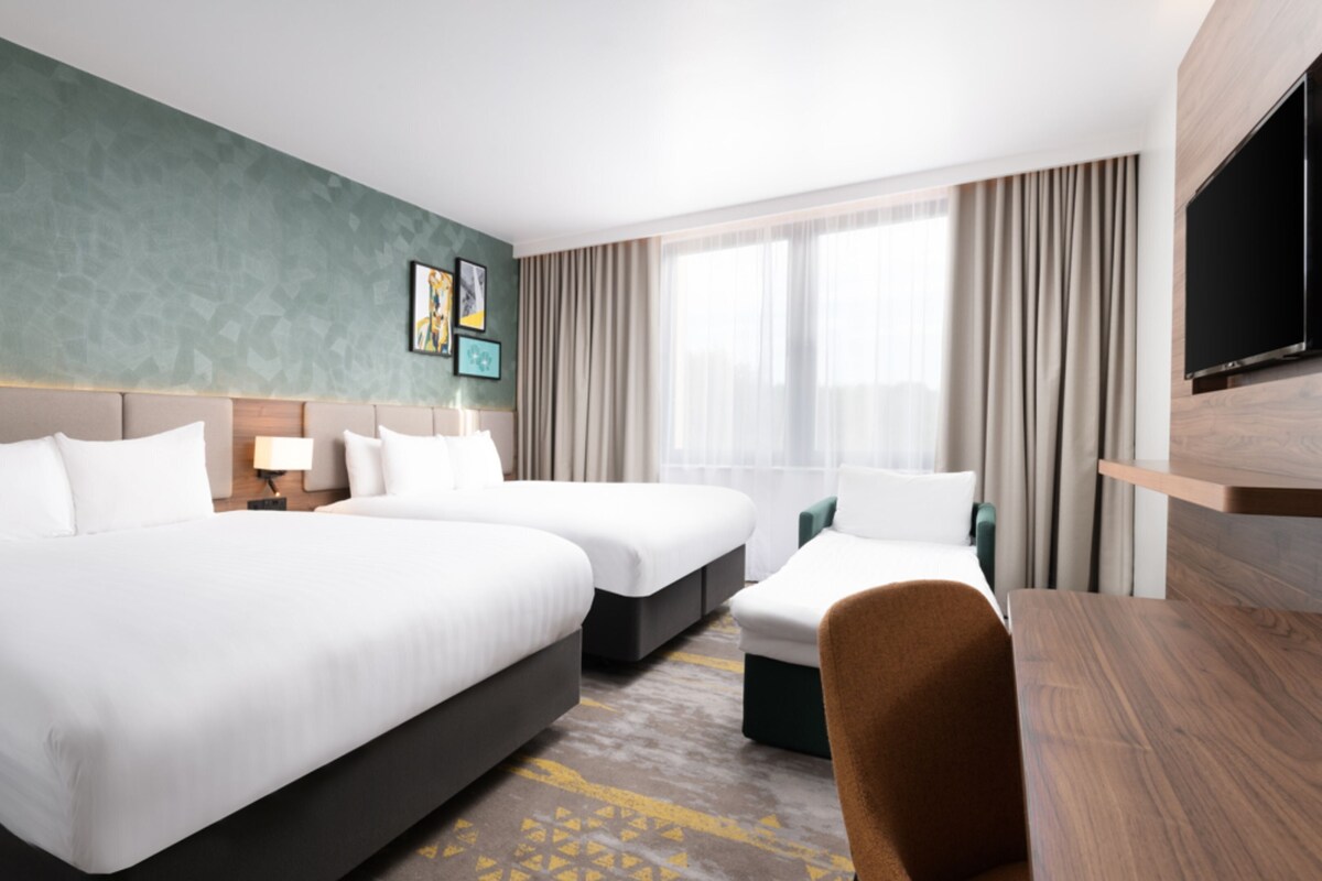 Une chambre d’hôtel avec deux lits, un bureau, une télévision et une grande fenêtre avec des rideaux.