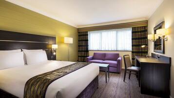 A hotel room with a large bed, a desk, a chair, a sofa, and a window with curtains.