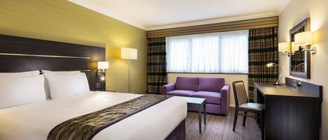 A hotel room with a large bed, a desk, a chair, a sofa, and a window with curtains.