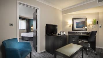 Een hotelkamer met een bed, een televisie, een bureau met stoel, een koffiezetapparaat en een schilderij aan de muur.
