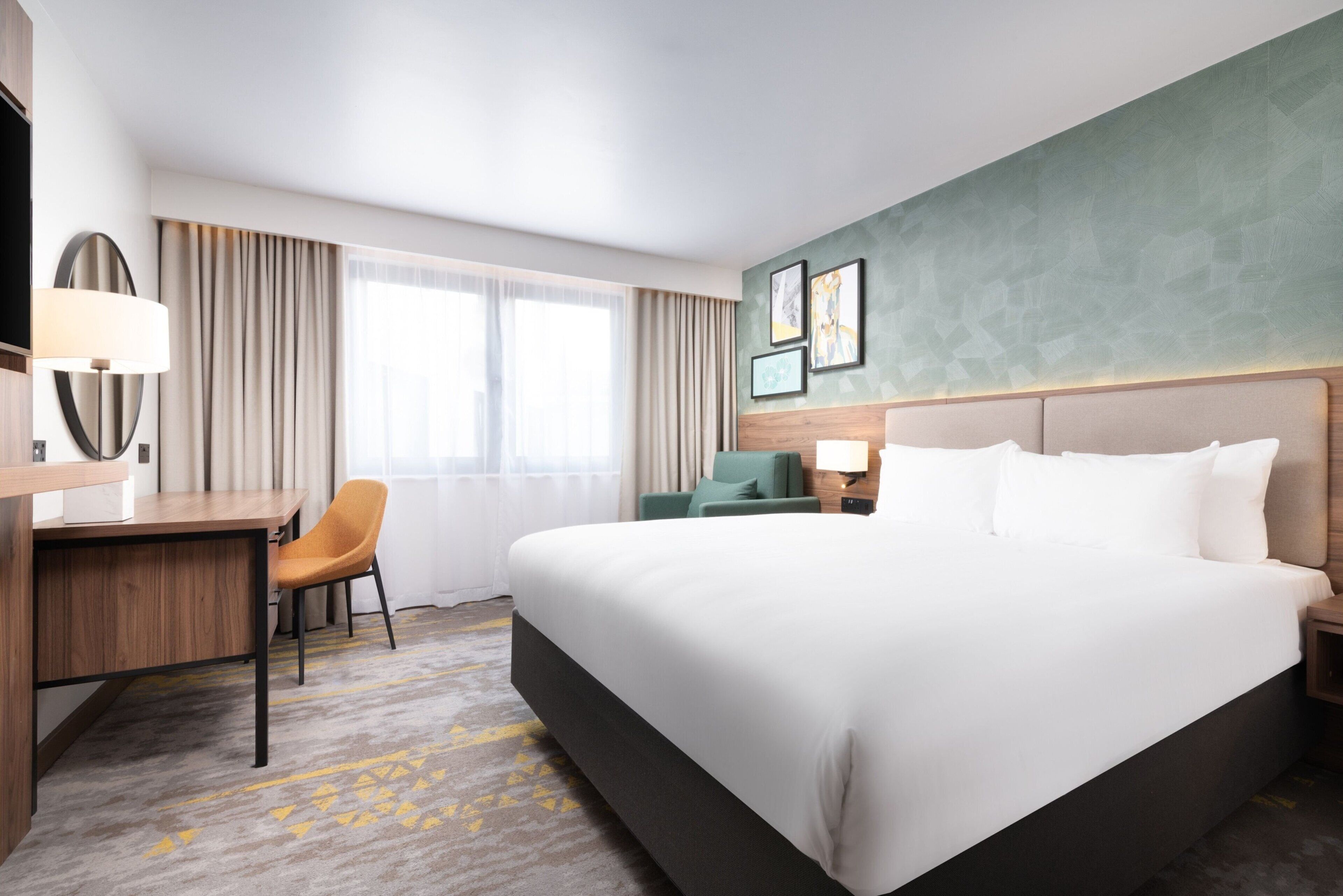 A hotel room with a large bed, a desk, a chair, and a window with curtains.