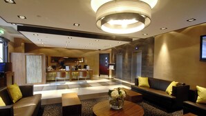 A hotel lobby with a reception desk, seating area, and a modern chandelier.
