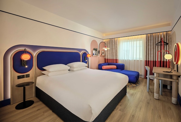 A modern hotel room with a large bed, a desk, and a seating area.