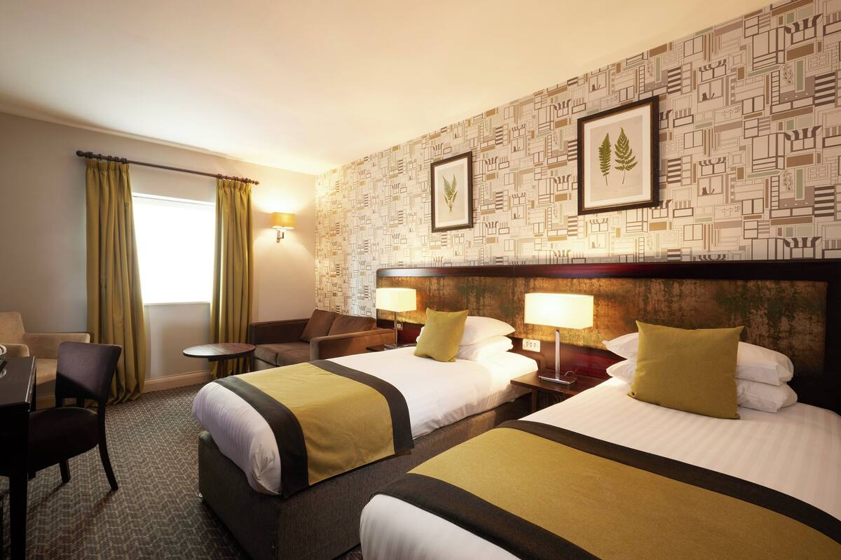 A hotel room with two beds, a desk, and a chair.