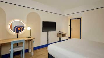 Una habitación de hotel con una cama, un escritorio con una silla, un televisor y una puerta.