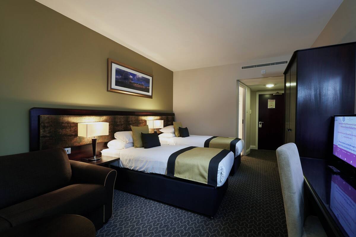 A hotel room with two beds, a desk, a chair, a TV, and a framed picture on the wall.