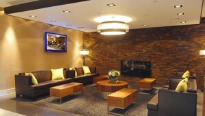 A modern lobby with a sofa set, wooden coffee tables, and a TV mounted on a brick wall.