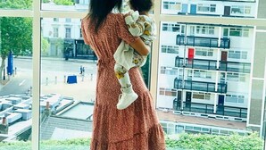 A woman holding a child in a room with large windows overlooking a cityscape.