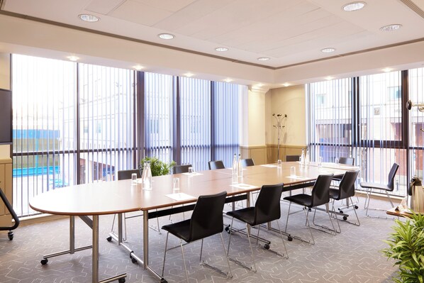 A conference room with a large table, black chairs, and large windows with blinds. - lyf Chelsea London (London)