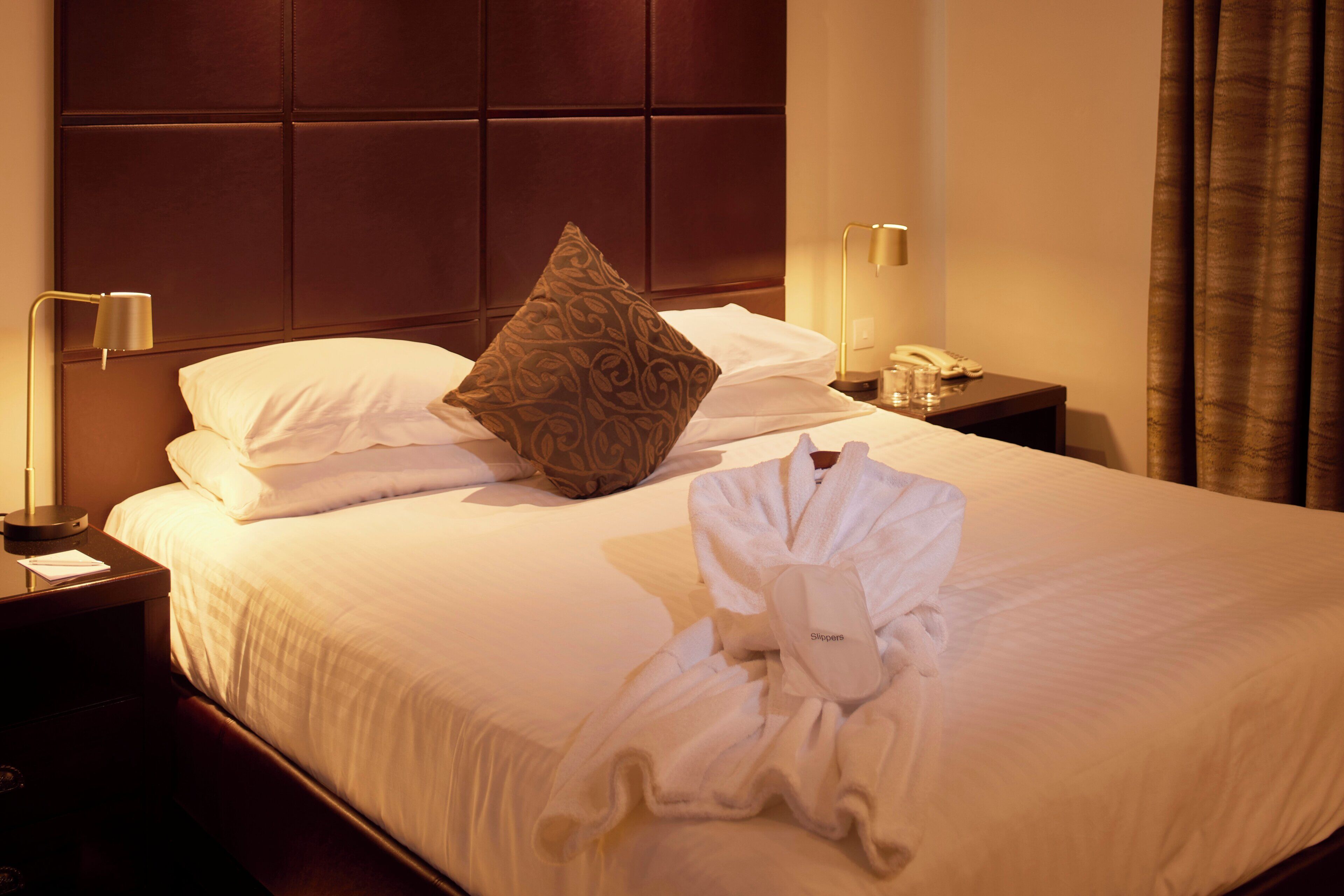 Une chambre d’hôtel avec un lit bien fait, un oreiller, un peignoir, une table de chevet avec une lampe et un téléphone.
