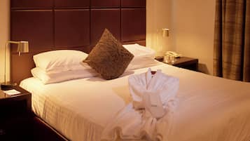 Een hotelkamer met een net opgemaakt bed, een kussen, een badjas, een nachtkastje met een lamp en een telefoon.
