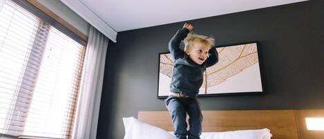 Niño saltando sobre una cama en una habitación de hotel con un ventanal grande y una obra de arte en la pared.