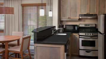 A modern kitchen with a dining area, featuring a round table, chairs, a built-in oven, a microwave, and wooden cabinets.