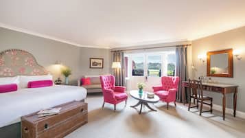 Un dormitorio con una cama grande, dos sillones rosa, un escritorio de madera y vistas al exterior.