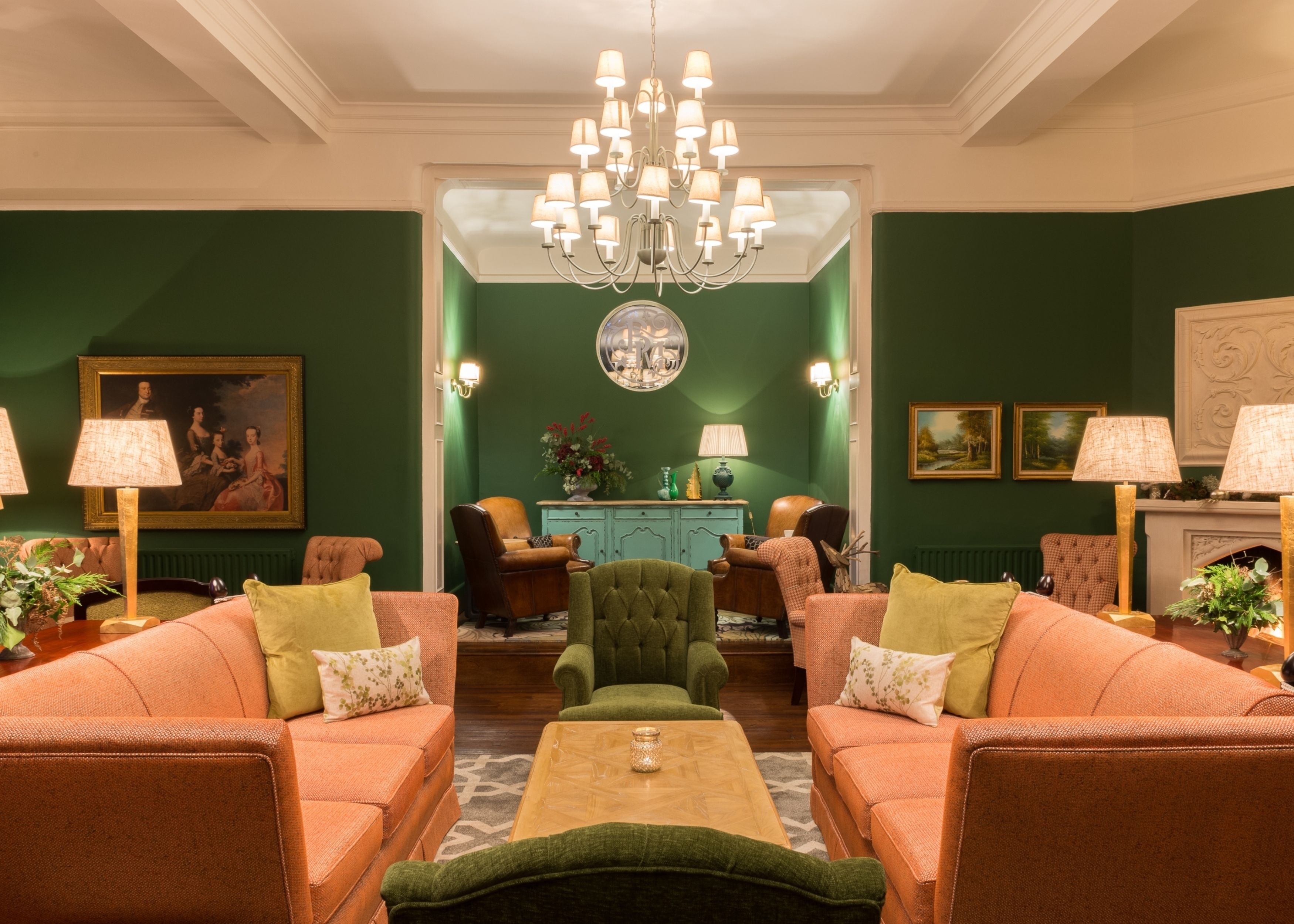 Une pièce avec deux canapés placés face à face, une table basse au centre, un lustre, une cheminée et un mur d’accent de couleur verte.