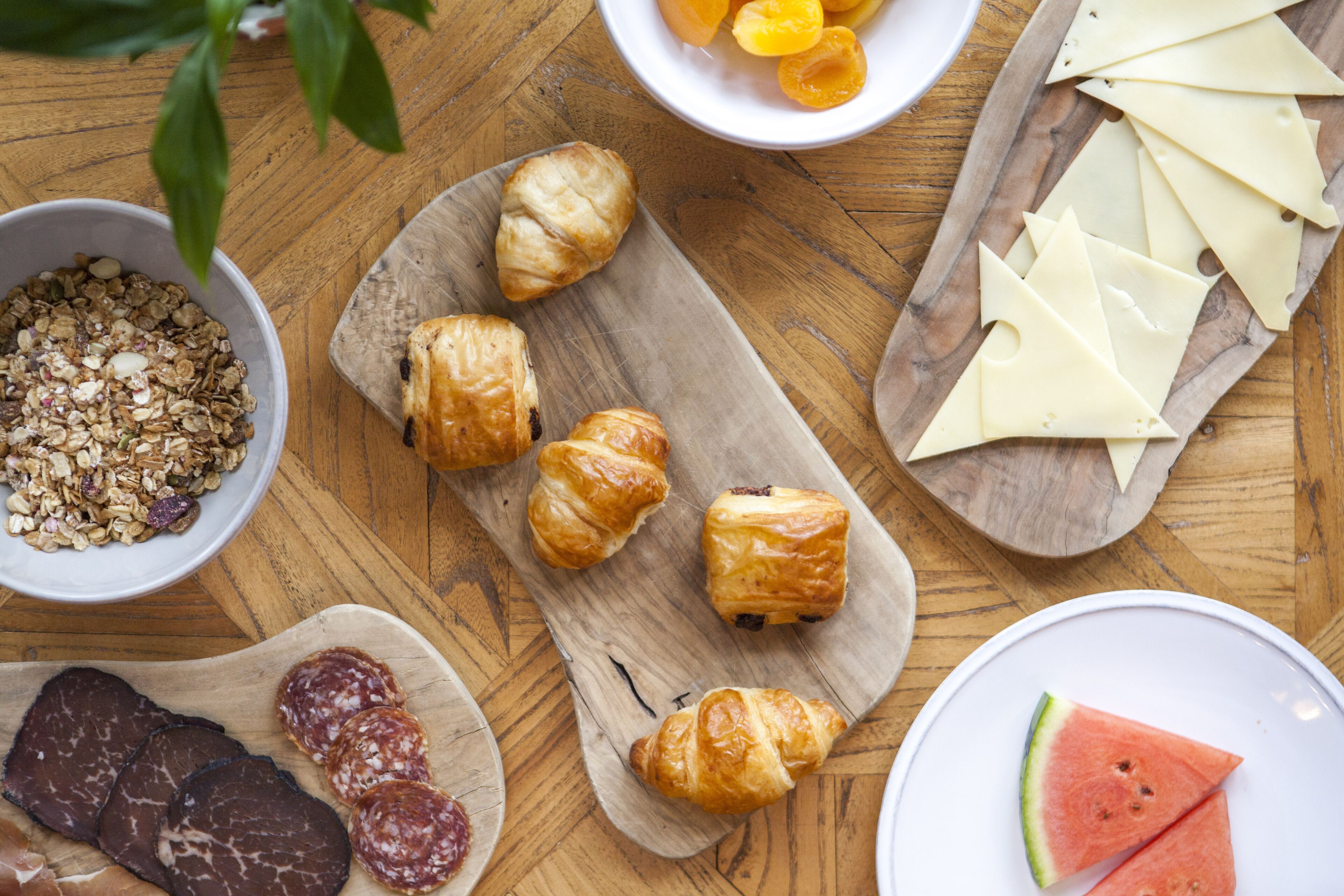 A wooden table with various food items including croissants, cheese, and watermelon slices.